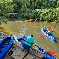 Rodzina w kajakach na rzece, przygotowująca się do spływów kajakowych Prosną. Zielone brzegi i słoneczny dzień.